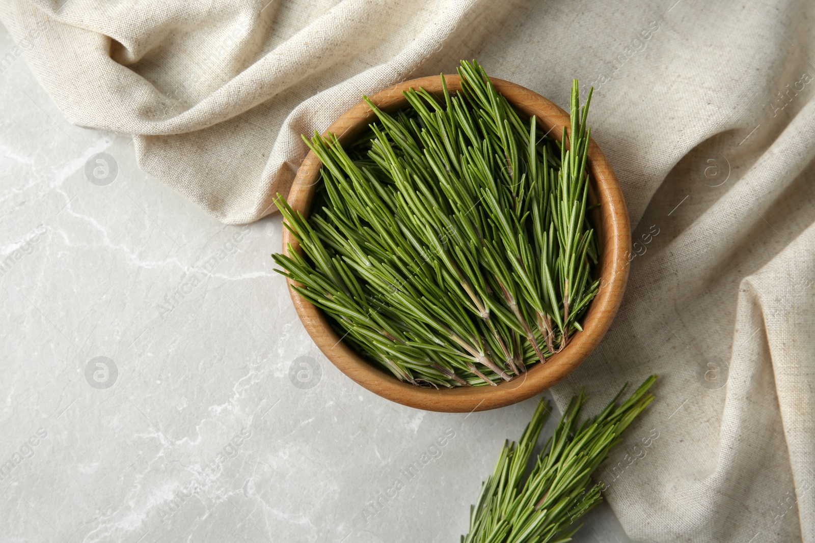 Photo of Bowl with fresh rosemary twigs on grey marble background, flat lay