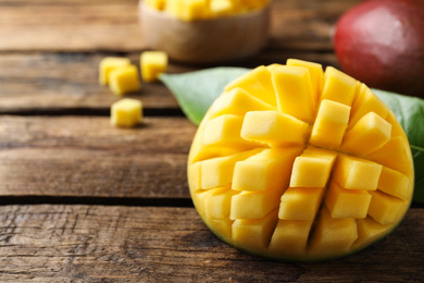 Half of ripe mango cut into cubes on wooden table, space for text