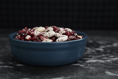 Photo of Bowl with dry kidney beans on black textured table, closeup