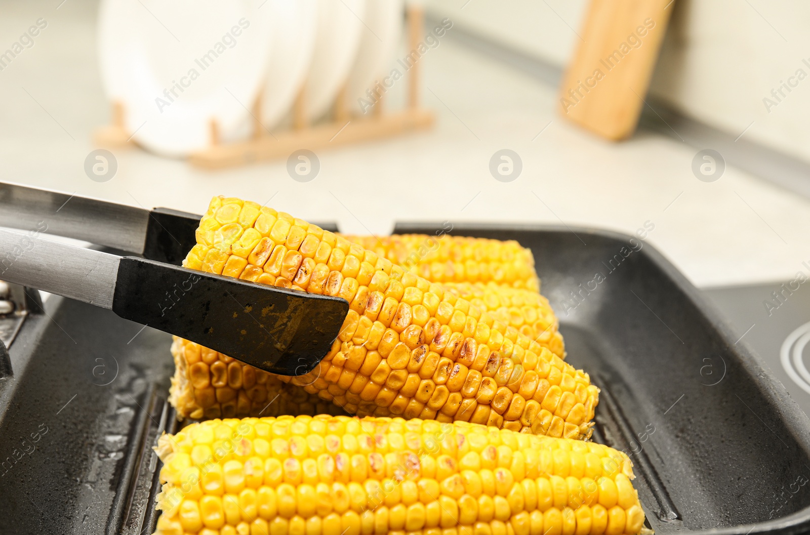 Photo of Taking corn from grill pan with tongs in kitchen, closeup