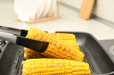 Photo of Taking corn from grill pan with tongs in kitchen, closeup