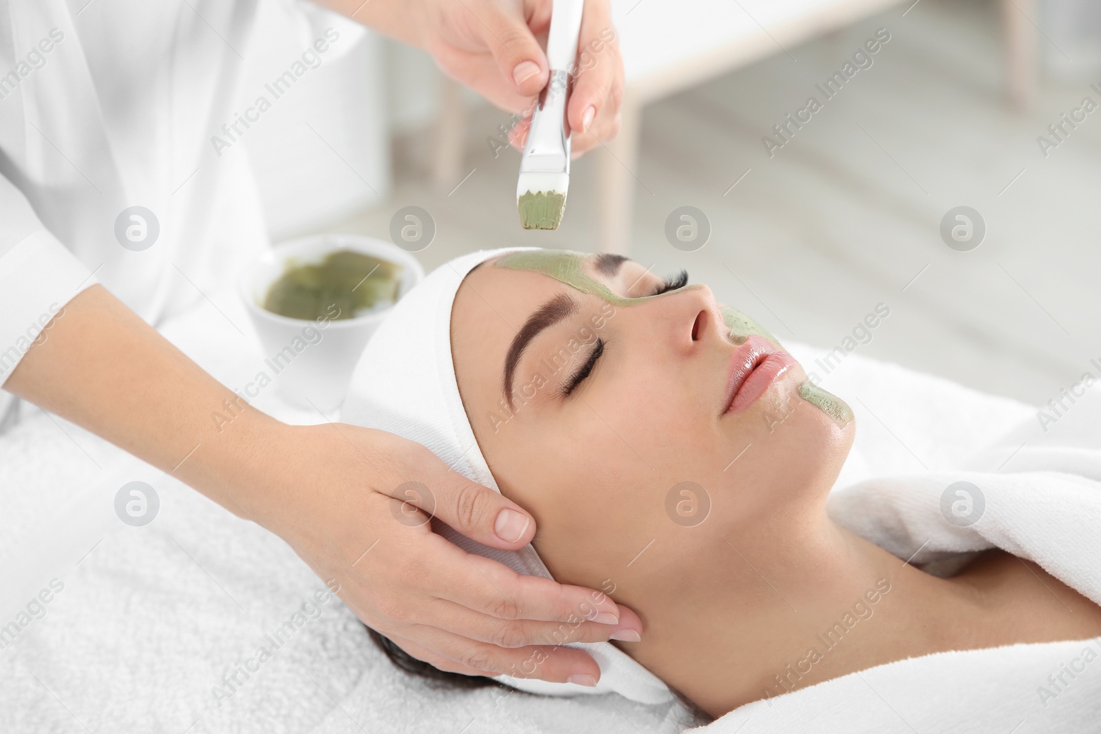 Photo of Cosmetologist applying mask on client's face in spa salon