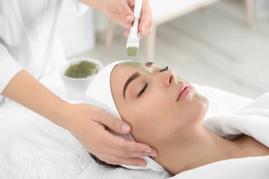 Photo of Cosmetologist applying mask on client's face in spa salon