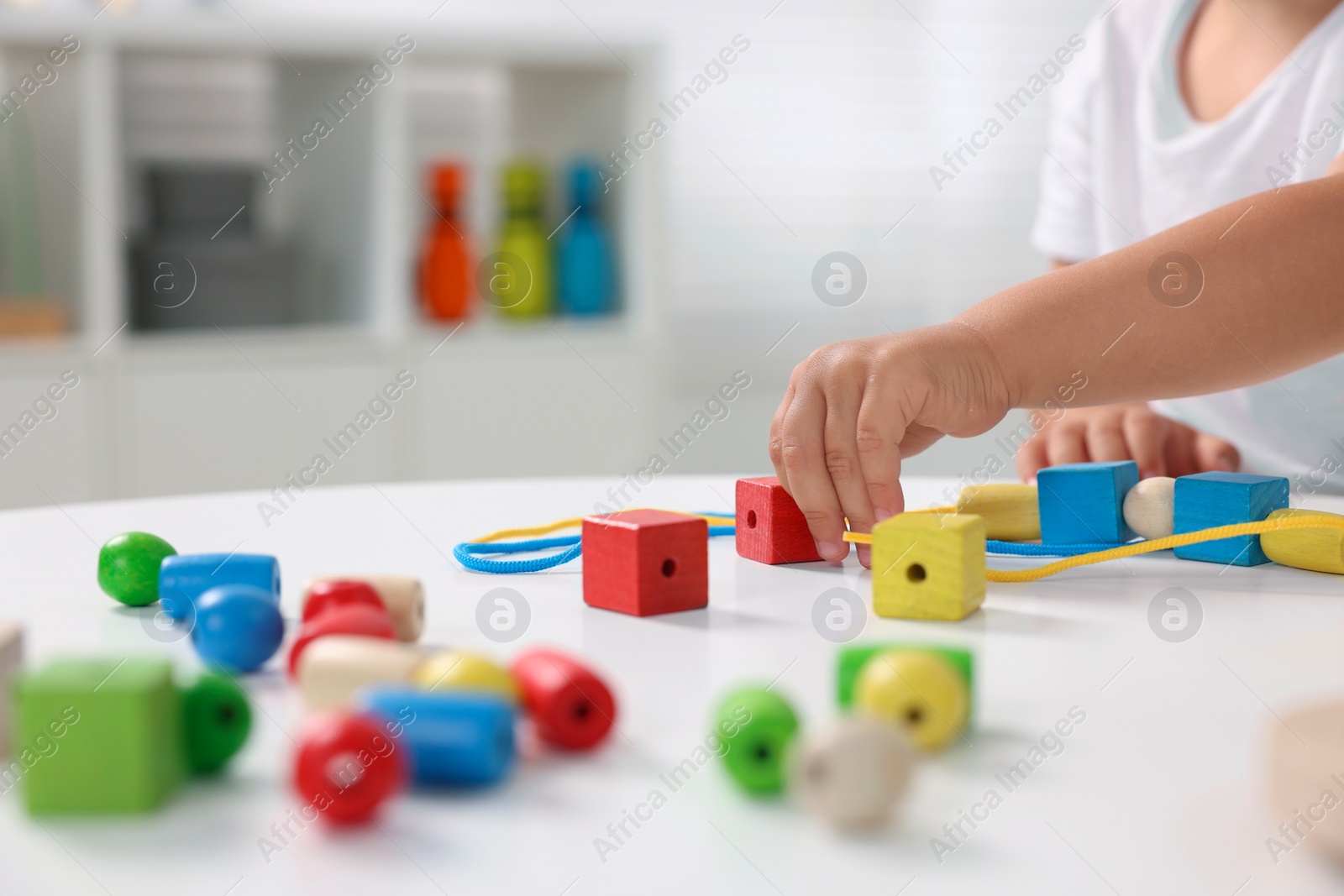 Photo of Motor skills development. Little boy playing with wooden pieces and string for threading activity at white table indoors, closeup