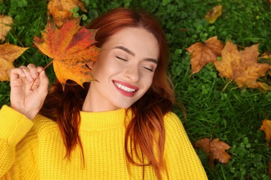 Photo of Smiling woman lying on grass with autumn leaf, top view