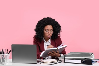 Photo of Stressful deadline. Tired woman working at white desk against pink background