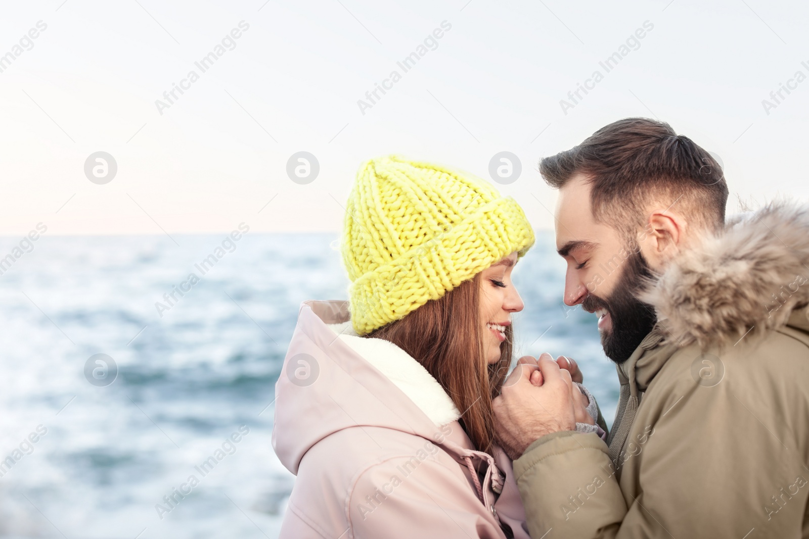 Photo of Lovely young couple holding hands near sea. Space for text
