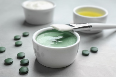 Freshly made spirulina in bowl, pills and brush on light grey table