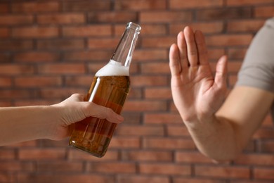 Photo of Man refusing to drink beer near red brick wall, closeup. Alcohol addiction treatment