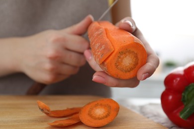 Photo of Woman peeling fresh carrot with knife at table indoors, closeup