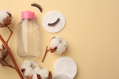 Photo of Bottle of makeup remover, cotton flowers, pads and false eyelashes on yellow background, flat lay. Space for text