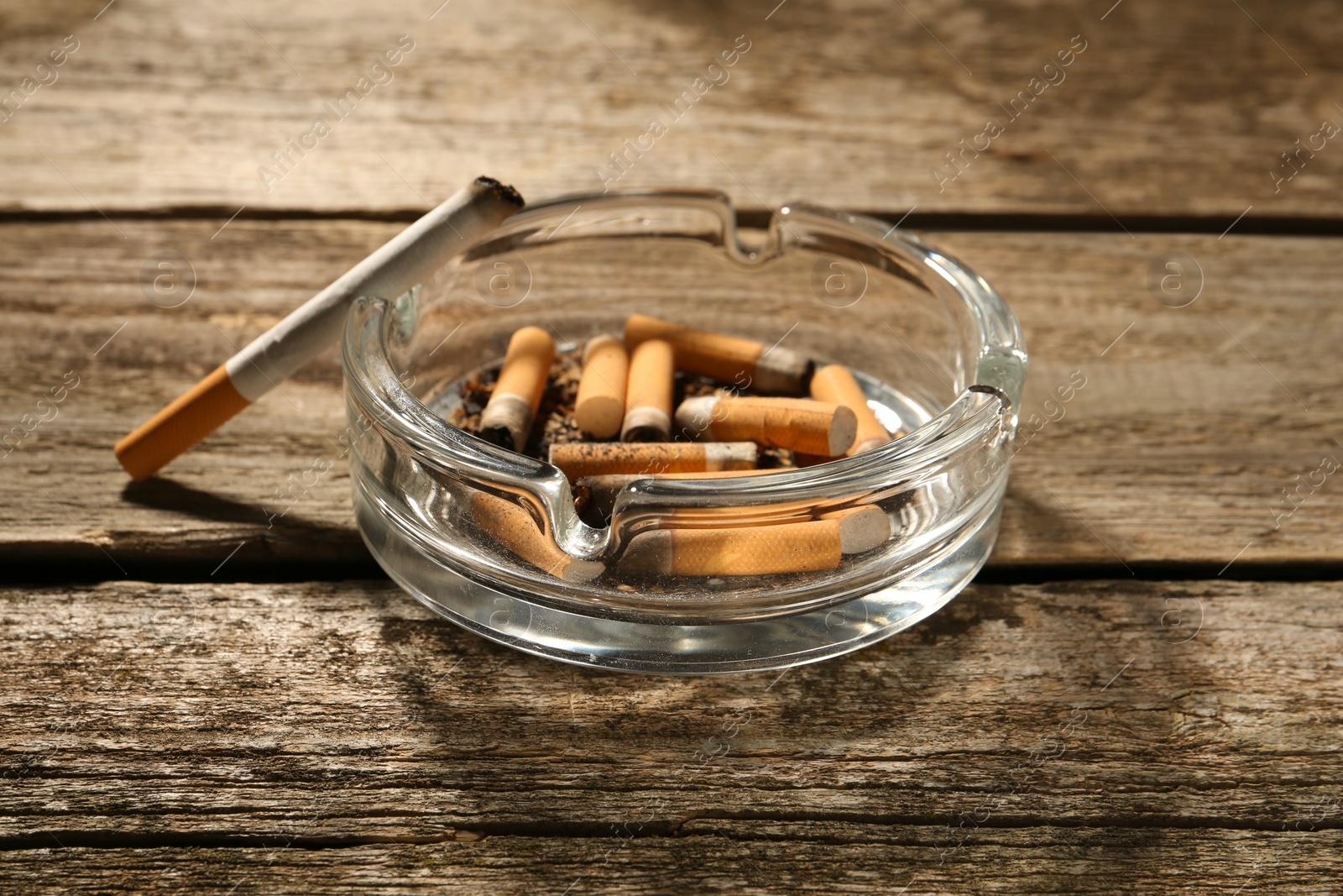 Photo of Glass ashtray with cigarette stubs on wooden table