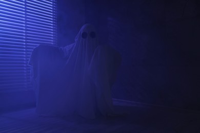 Photo of Creepy ghost. Woman covered with sheet near window in blue light, space for text