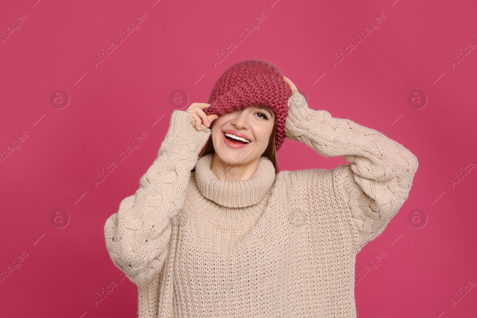 Photo of Young woman wearing warm sweater and hat on crimson background. Winter season