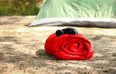 Photo of Rolled sleeping bag with binoculars near tent on beach