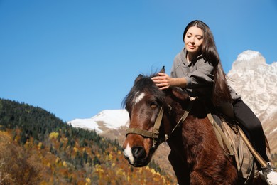 Photo of Young woman riding horse in mountains on sunny day. Beautiful pet