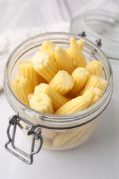 Tasty fresh yellow baby corns in glass jar on white tiled table