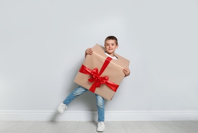 Cute little boy dressed as gift box near white wall. Christmas suit