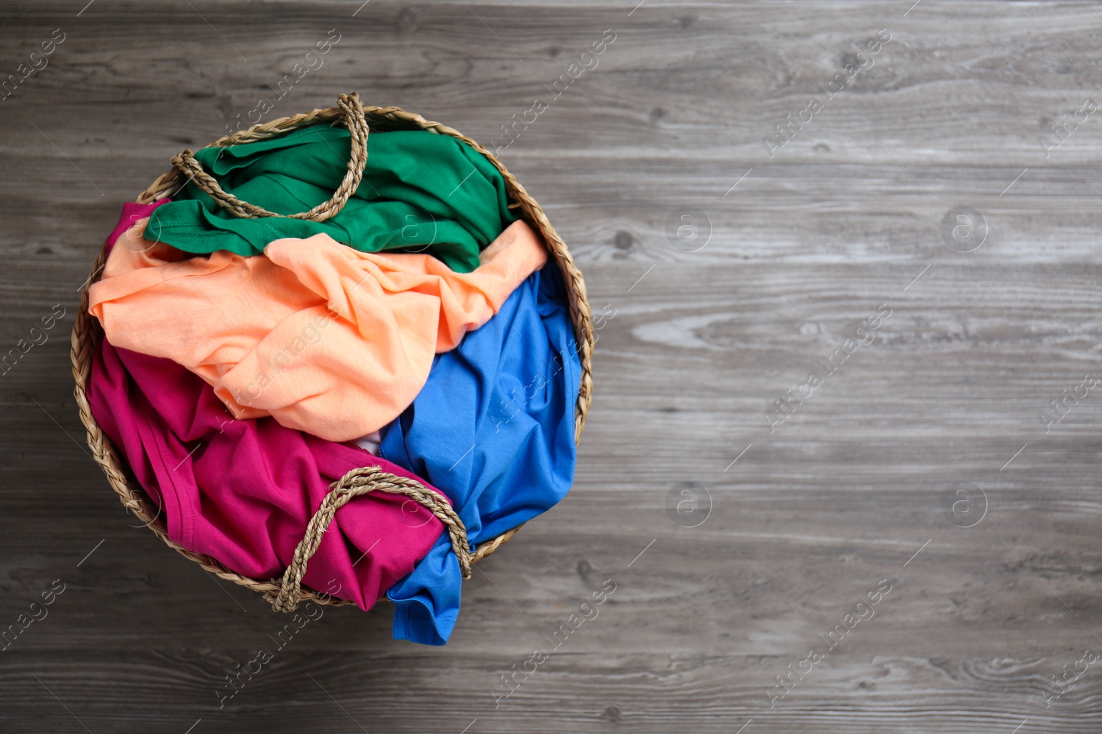 Photo of Wicker laundry basket with different clothes on wooden background, top view. Space for text