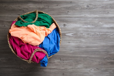 Photo of Wicker laundry basket with different clothes on wooden background, top view. Space for text