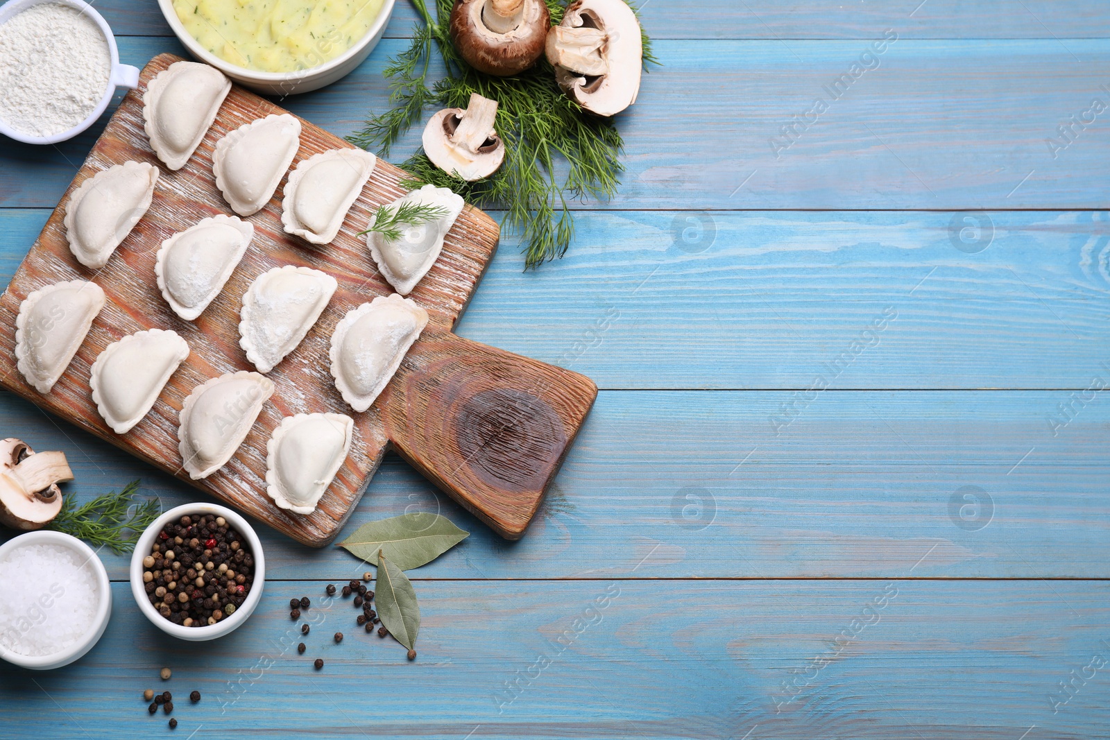 Photo of Raw dumplings (varenyky) and ingredients on light blue table, flat lay. Space for text