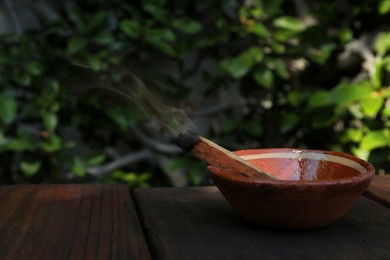 Palo santo stick in bowl on wooden table outdoors, space for text