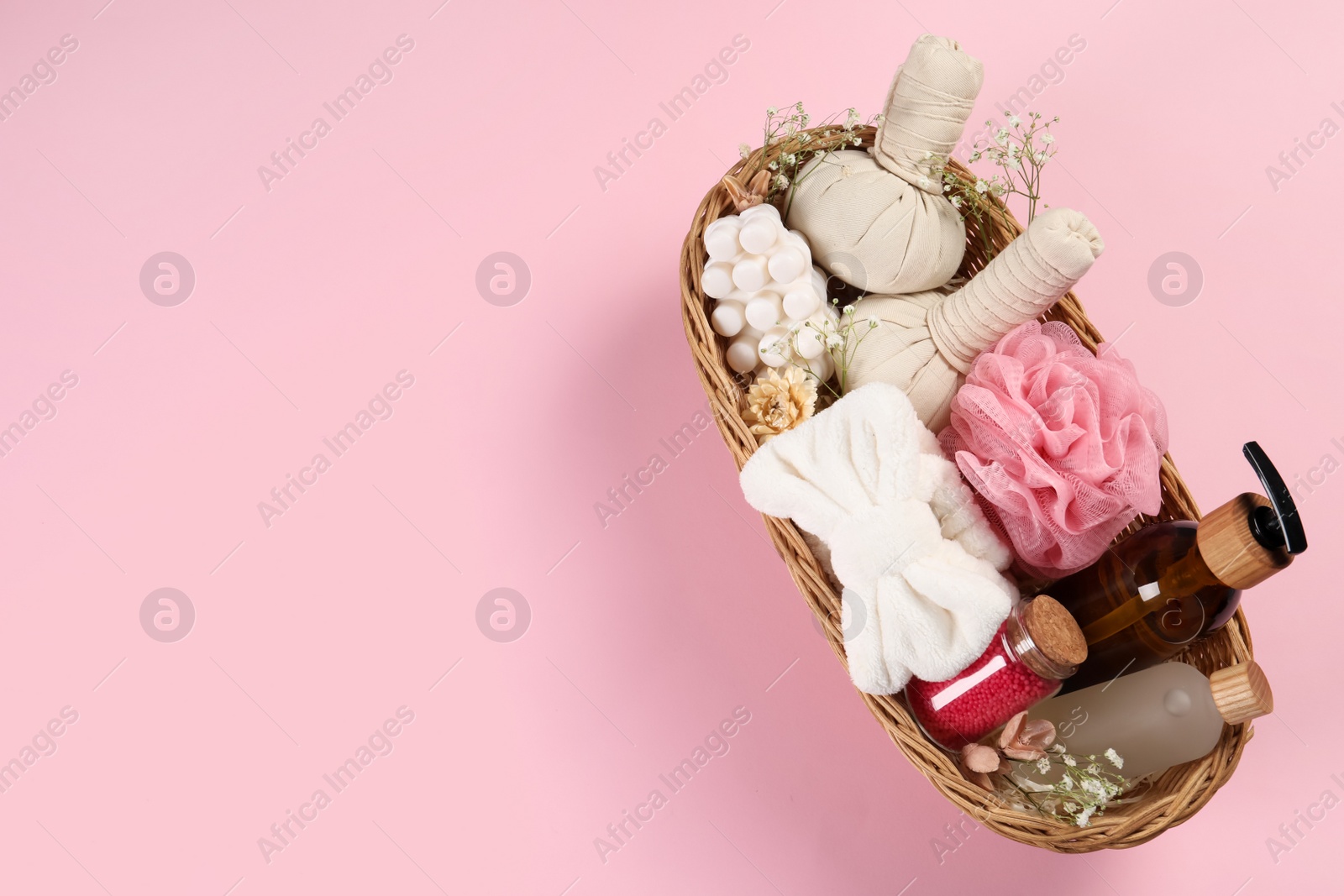 Photo of Spa gift set with different products in wicker basket on pink background, top view. Space for text