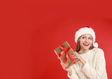 Photo of Happy young woman in Santa hat with Christmas gift on red background. Space for text