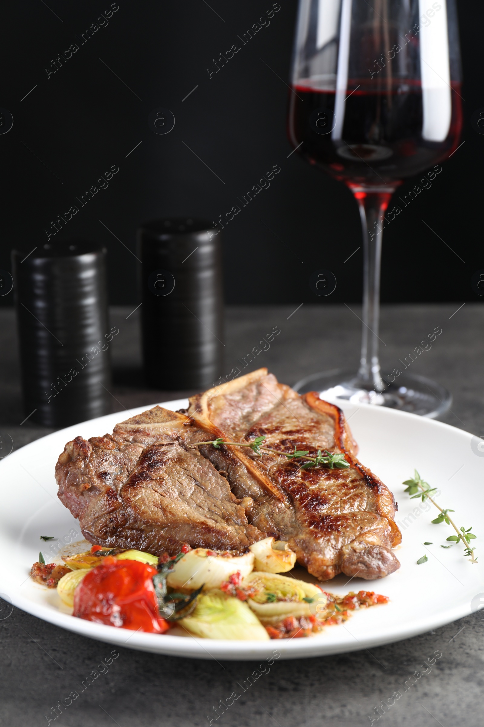 Photo of Delicious fried beef meat, vegetables and glass of wine on grey table