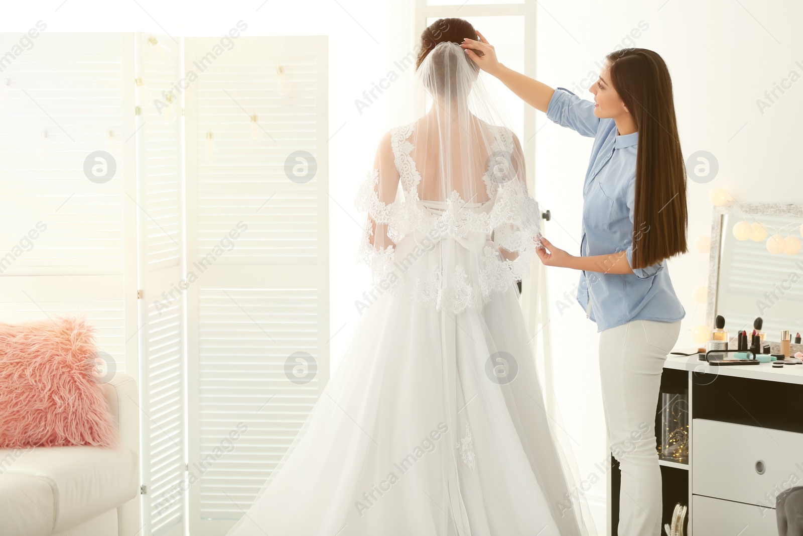 Photo of Fashion stylist preparing bride before her wedding in room