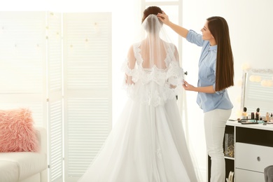 Fashion stylist preparing bride before her wedding in room