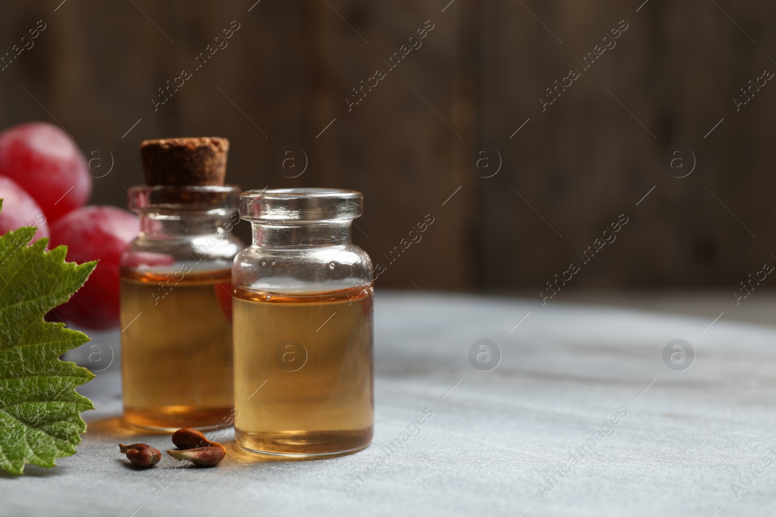 Photo of Bottles of natural grape seed oil on grey table, space for text. Organic cosmetic