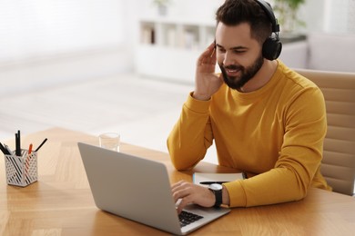 Photo of Young man in headphones watching webinar at table in room