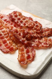 Photo of Board with fried bacon slices on grey textured table, closeup