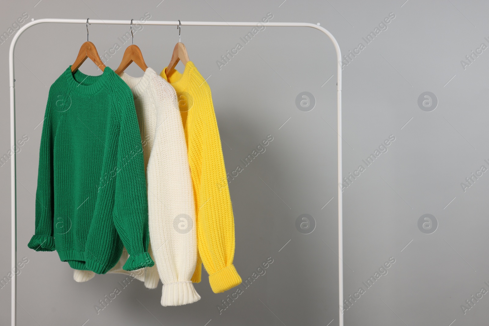 Photo of Rack with different warm sweaters on light grey background. Space for text