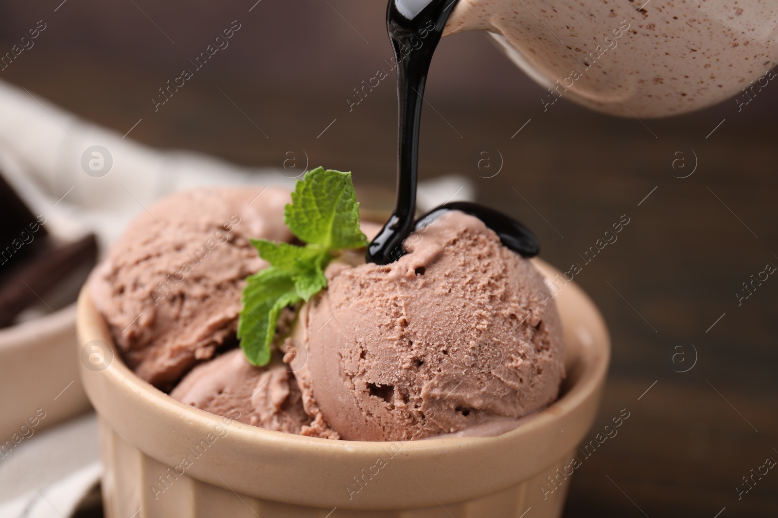 Photo of Pouring chocolate syrup onto ice cream on blurred background, closeup