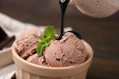 Pouring chocolate syrup onto ice cream on blurred background, closeup