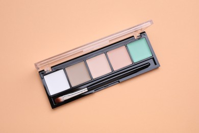 Colorful contouring palette with brush on beige background, top view. Professional cosmetic product