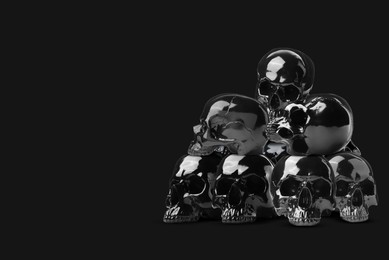 Image of Pile of shiny human skulls on black background, space for text