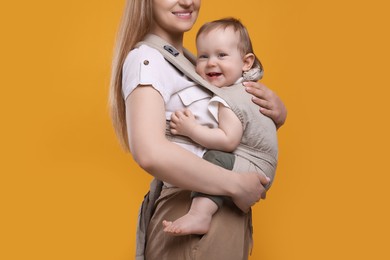 Photo of Mother holding her child in sling (baby carrier) on orange background, closeup