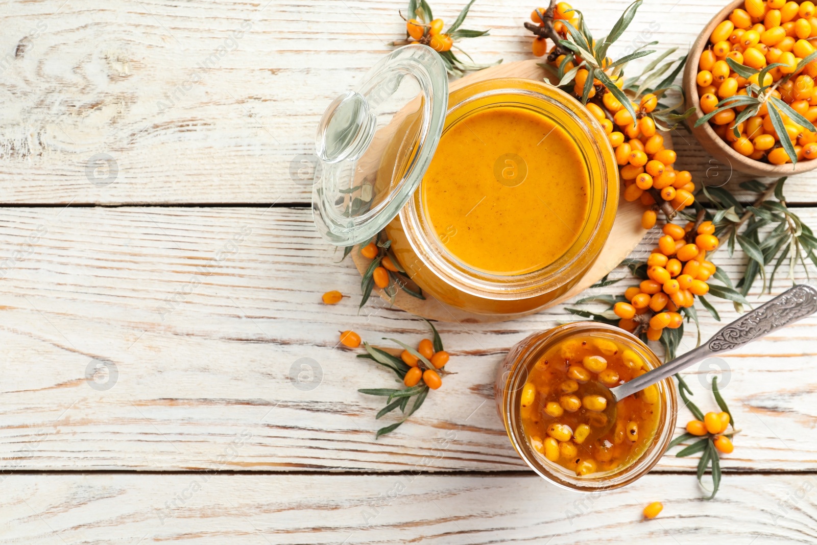 Photo of Delicious sea buckthorn jam and fresh berries on white wooden table, flat lay. Space for text