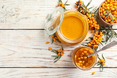 Photo of Delicious sea buckthorn jam and fresh berries on white wooden table, flat lay. Space for text