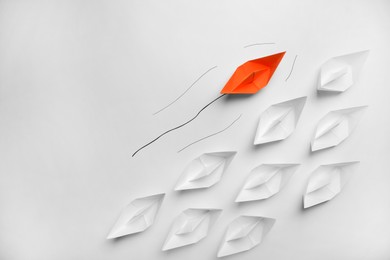 Photo of Orange paper boat floating past others on white background, flat lay with space for text. Uniqueness concept