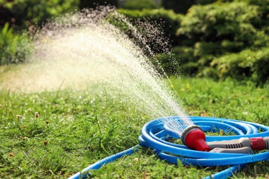 Photo of Water spraying from hose on green grass outdoors