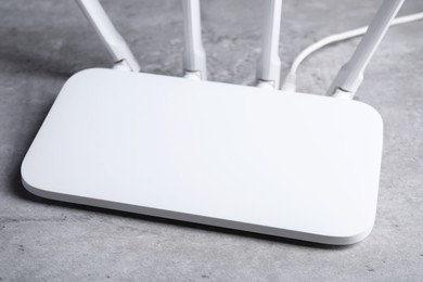 Photo of New white Wi-Fi router on grey textured table, closeup