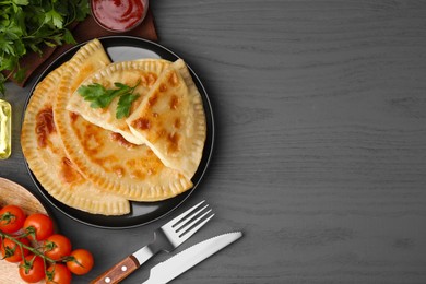 Photo of Delicious fried chebureki with cheese, parsley and ingredients served on grey wooden table, flat lay. Space for text