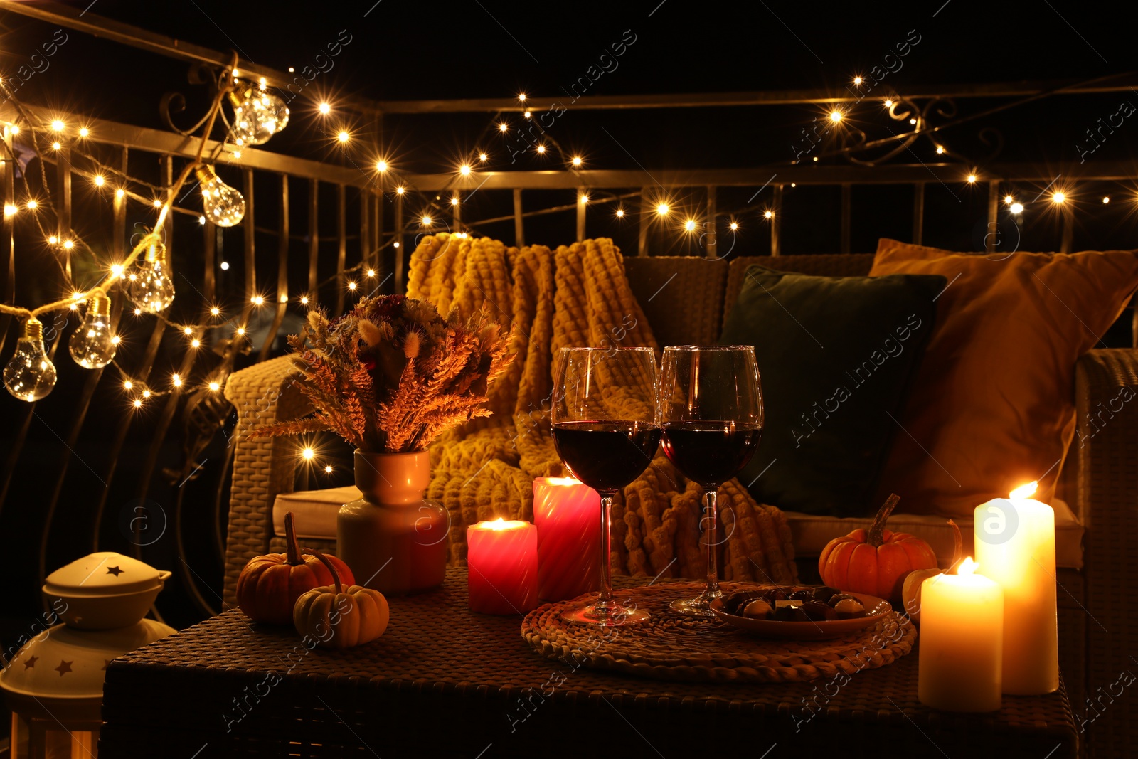 Photo of Glasses of wine, burning candles and autumn decor on outdoor terrace in evening