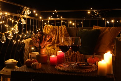 Glasses of wine, burning candles and autumn decor on outdoor terrace in evening