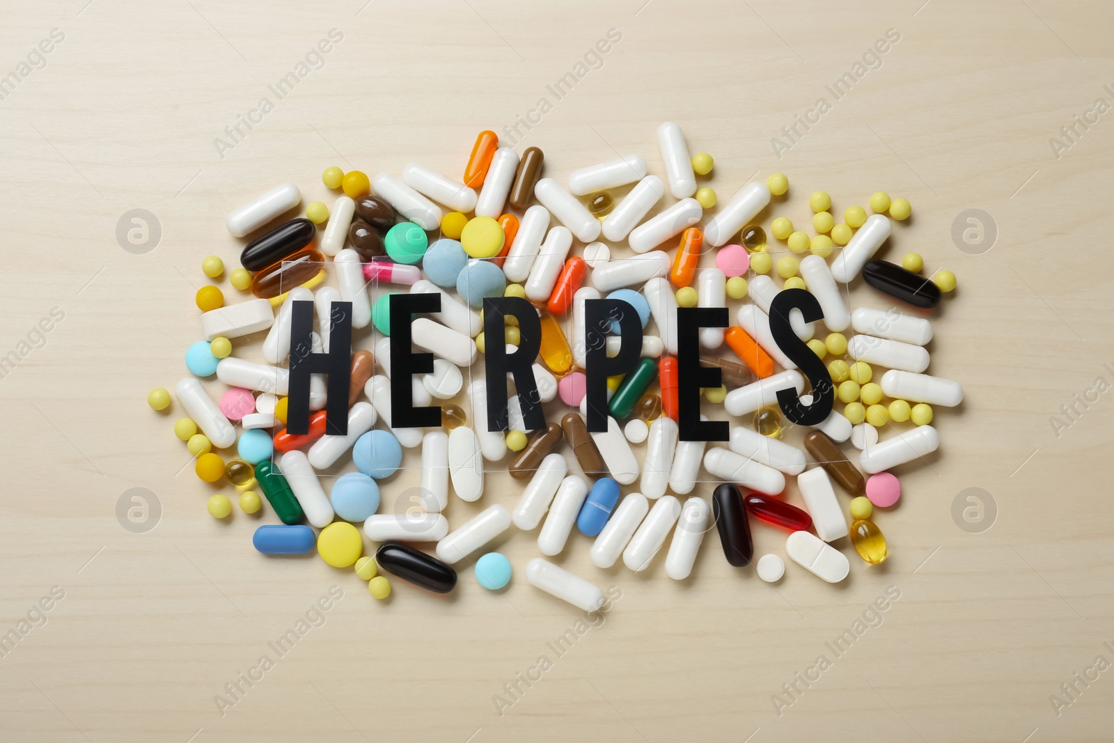 Photo of Word Herpes and different pills on wooden table, flat lay