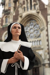 Young nun with Bible near cathedral outdoors